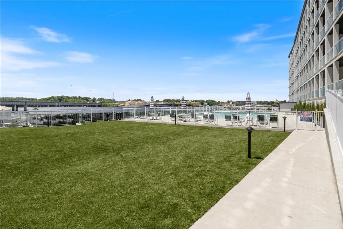 A lively exterior scene featuring a green lawn, a sparkling community swimming pool, lounge chairs, and the building’s facade. The bright, open space suggests a fun atmosphere ideal for family gatherings, playtime, and relaxing under the sun.