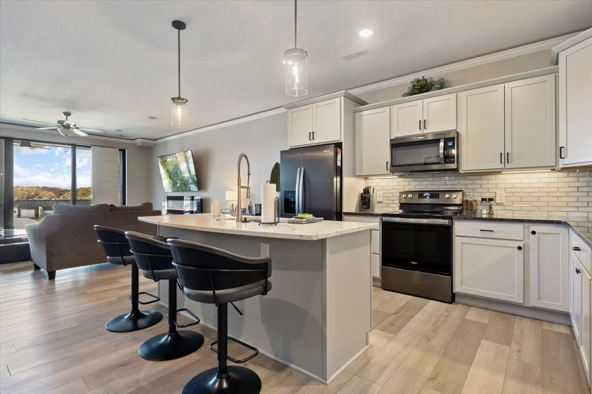 A contemporary kitchen with a spacious island, sleek black appliances, and large windows that let in ample light and offer scenic water views. Adjacent is a comfortable seating area, blurring the boundaries between cooking, socializing, and relaxing.