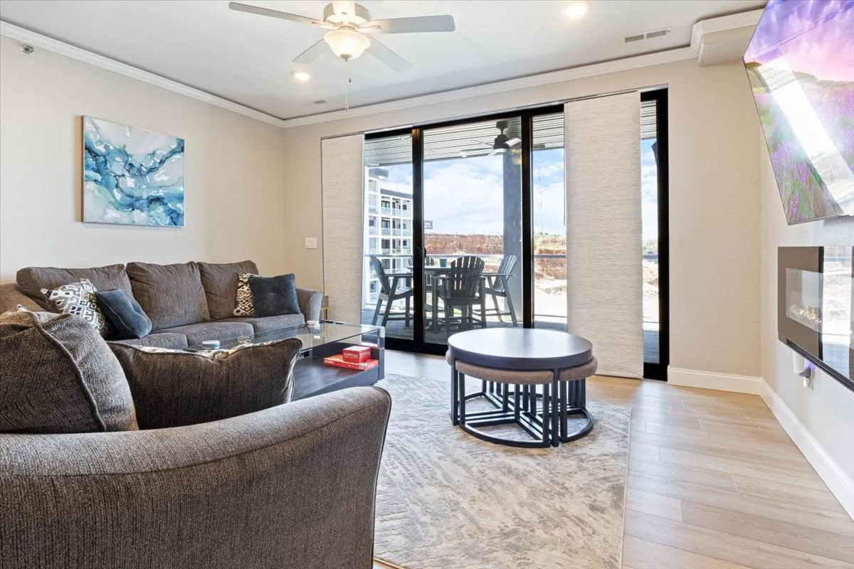 A welcoming living space with a comfortable gray sofa, a stylish coffee table, and large sliding glass doors that open up to the outdoors. Decorative wall art adds character, and the room is flooded with natural light. The layout encourages socializing and soaking up exterior views.