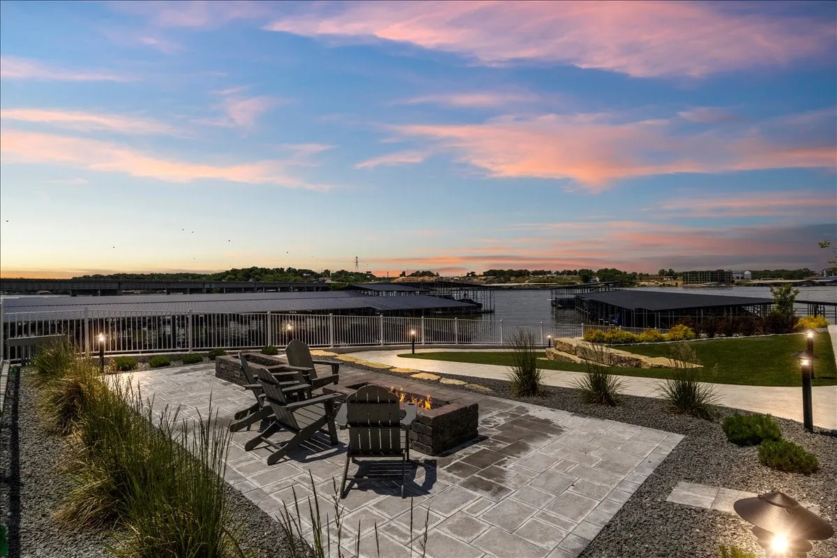 An inviting fire pit encircled by adirondack chairs, overlooking a serene water view and lush landscaped garden. The ambiance suggests cozy evening gatherings where guests can unwind and share stories as the sun sets.