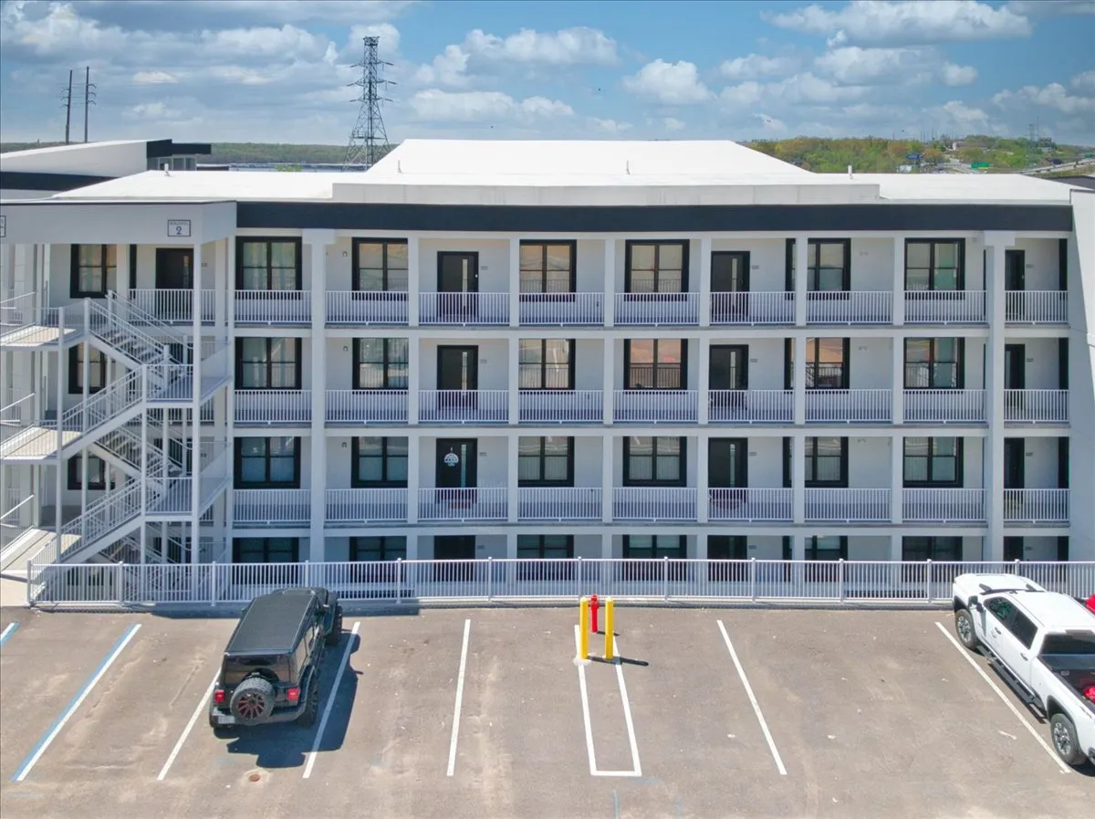 An exterior view of the multi-story building featuring balconies that overlook the area and a parking lot below. The building's architecture and outdoor spaces hint at the proximity to the lake and social opportunities, including gatherings on balconies and easy access to local attractions.