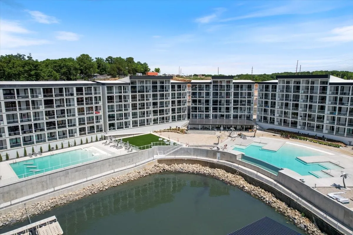 This exterior image showcases two sparkling swimming pools set against a waterfront backdrop, complemented by modern architecture and meticulously landscaped areas. The scene captures people enjoying the amenities through swimming, sunbathing, and casual outdoor gatherings.