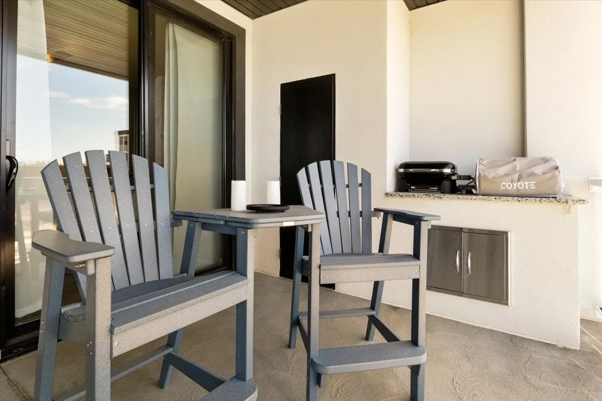 The image presents a set of inviting Adirondack chairs arranged around a small table next to a grill, positioned to take in the sunset views. The atmosphere is both intimate and social, ideal for relaxing or sharing a meal while watching the sky change colors.
