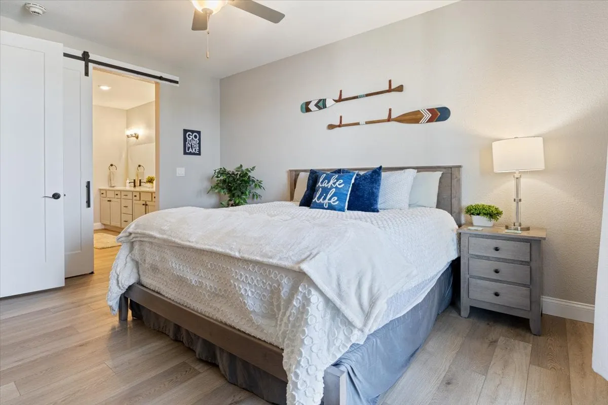 A cozy, peaceful bedroom with a comfortable bed dressed in decorative pillows, a wooden wall accent, and a lamp on the nightstand, creating a warm glow. The setting is intimate and inviting, perfect for unwinding after a long day.