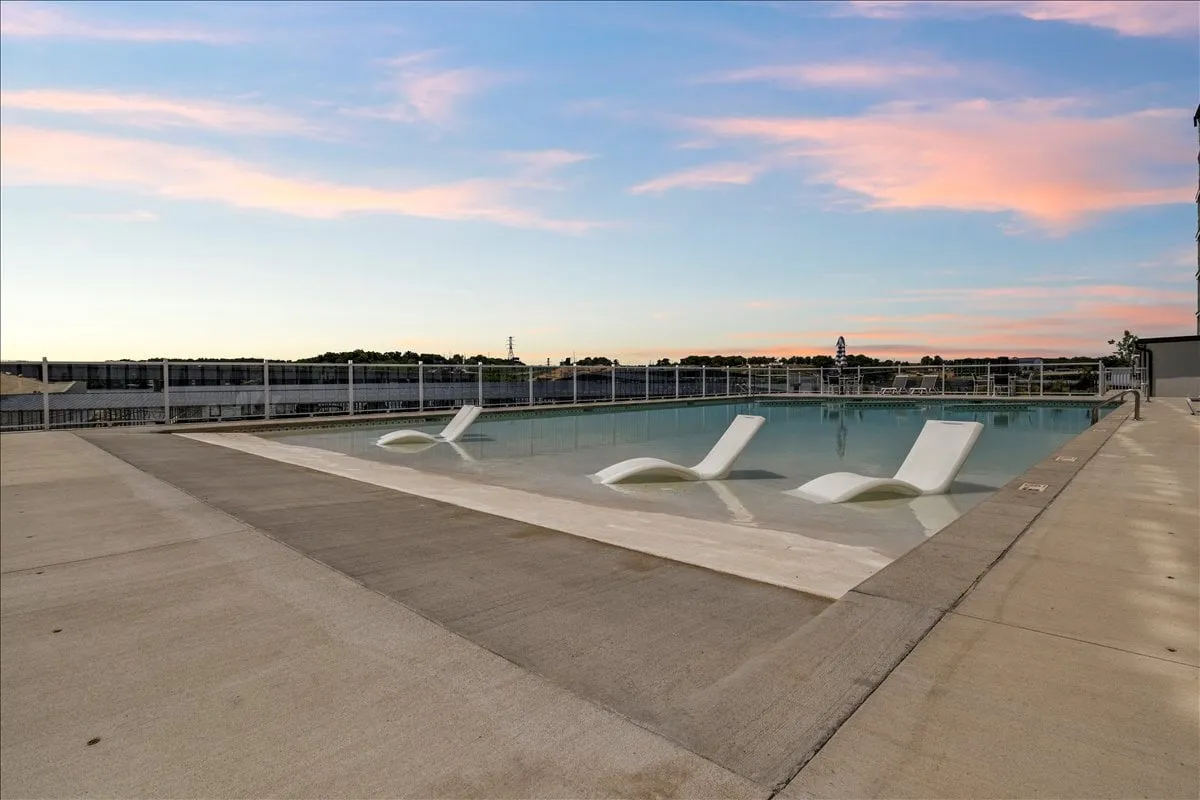 A vibrant outdoor swimming pool surrounded by inviting lounge chairs under an open sky. The pool area is tranquil and perfect for social gatherings, sunbathing, and unwinding with friends. The clear water and open vista evoke the carefree spirit of lakeside escapes.