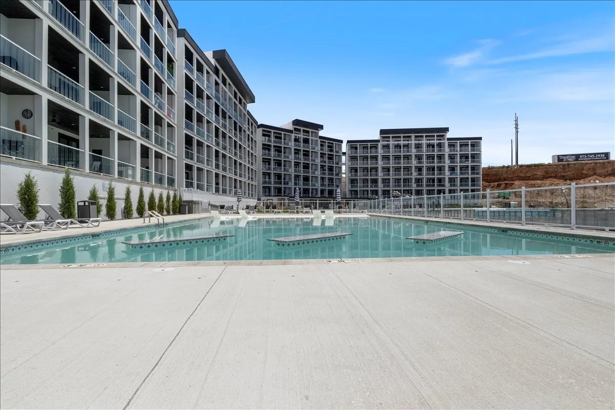 This exterior image features a sparkling swimming pool surrounded by lounge chairs and adjacent buildings, evoking a relaxed, vacation-like atmosphere. The pool area appears inviting for both social gatherings and peaceful relaxation, with plenty of space for guests to unwind.