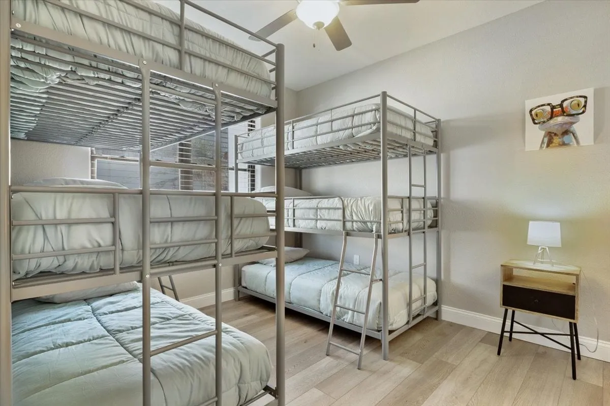 A playful and functional bedroom featuring bunk beds, a small nightstand with a lamp, and cheerful wall art. The space is designed to accommodate families or groups, balancing fun and comfort.